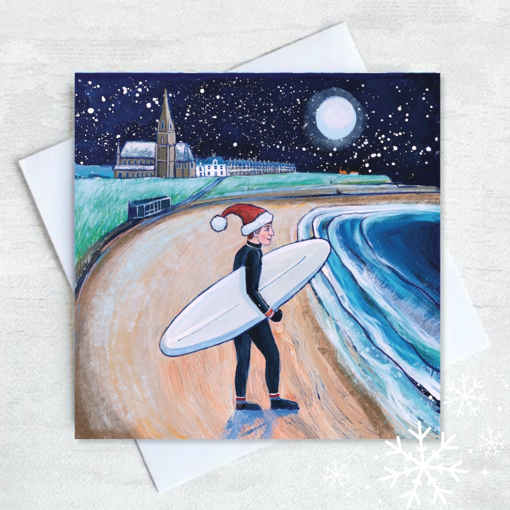 A cheerful surfer approaches the winter waves at Longsands Beach, Tynemouth, as snowflakes fall under a full moon illuminating the sandy beach. 