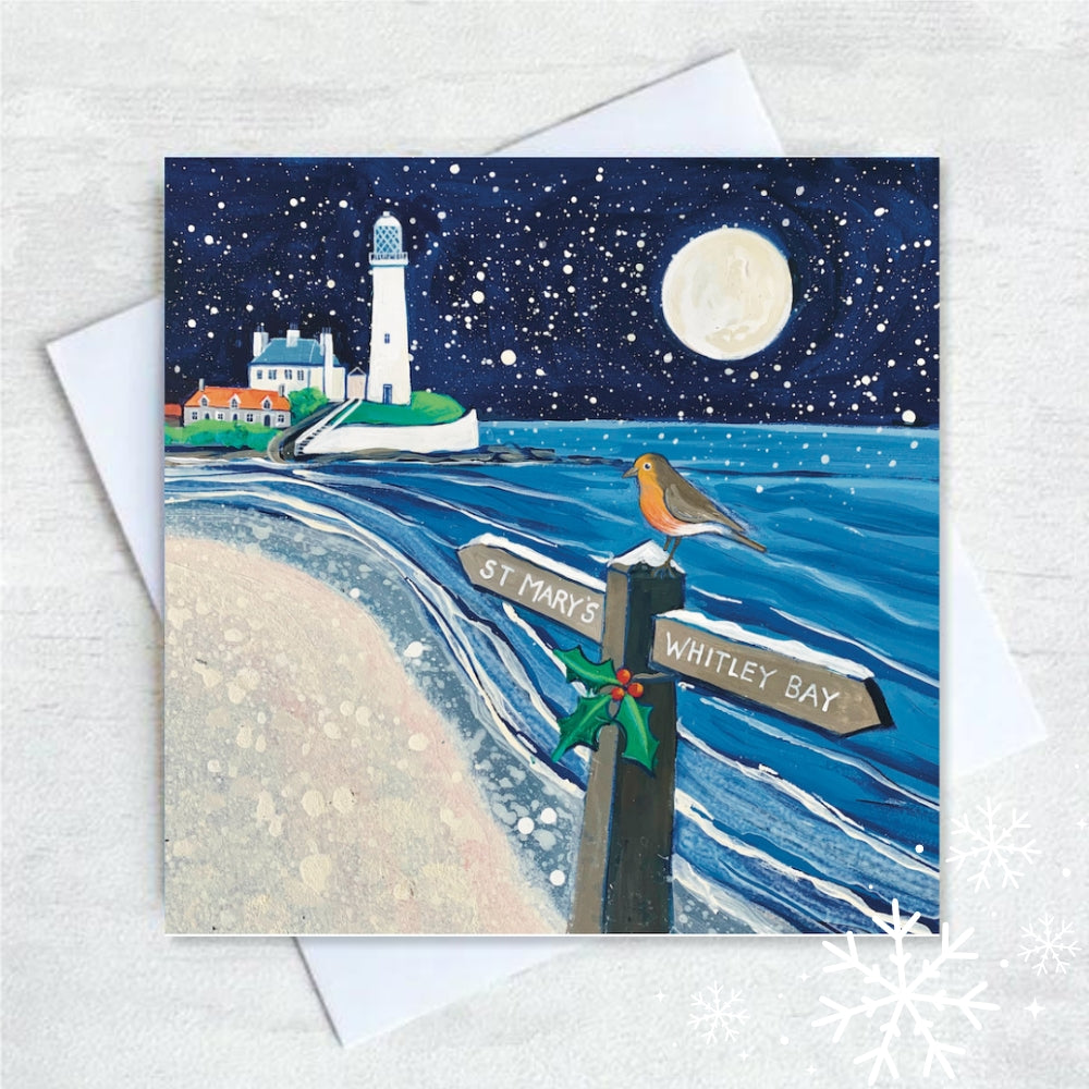 St. Mary&#39;s Lighthouse in Whitley bay is lit up by the full moon on a winter&#39;s night. Snow fills the dark sky and a robin perches on a signpost in the sandy shore reading Whitley Bay and St. Mary&#39;s. 