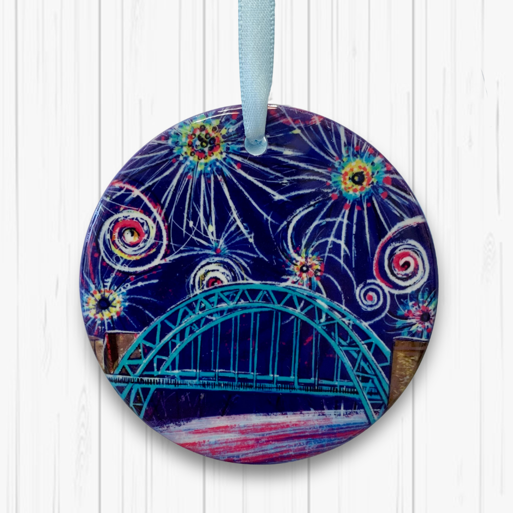 A circular ceramic decoration hung against a white background. It features the Tyne Bridge under a dark blue sky of colourful fireworks. 