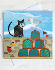 A coastal greetings card featuring a black cat in conversation with a cheeky seagull. They are on a harbour wall surrounded by lobster pots.