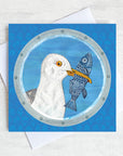 A coastal greetings card featuring a seagull with a fish in its beak.